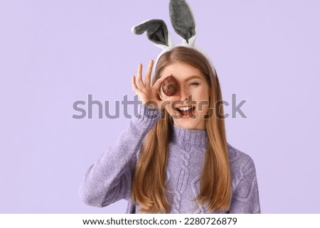 Young woman in bunny ears with Easter egg on lilac background