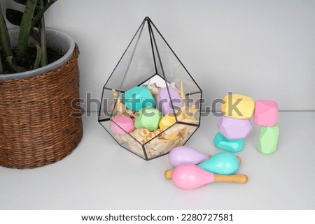 Children's wooden constructors in a glass florarium. Colored cubes of various shapes. Baby maracas. Green branch of houseplants.