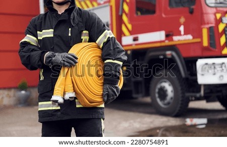 Outside near truck and with fire hose in hands. Woman in uniform is at work in department. Royalty-Free Stock Photo #2280754891