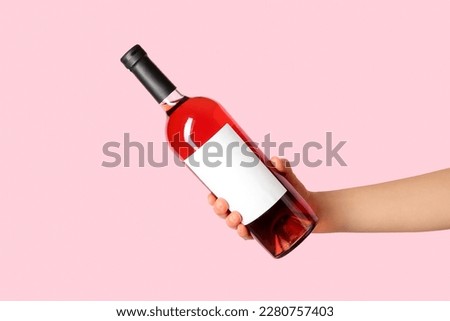 Female hand holding bottle of red wine on pink background Royalty-Free Stock Photo #2280757403