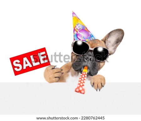 French Bulldog puppy blows into party whistle, shows signboard with labeled "sale" and looks above empty white banner. isolated on white background