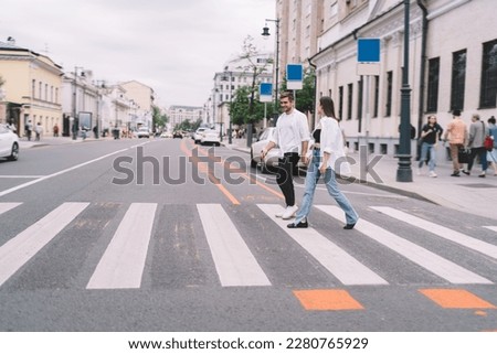 Full body of young man and woman in casual clothes holding hands while crossing street on crosswalk during date in city Royalty-Free Stock Photo #2280765929
