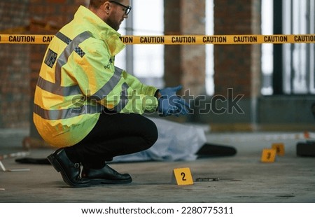 Wearing gloves. Male detective is collecting evidence in a crime scene near dead body on the construction site. Royalty-Free Stock Photo #2280775311