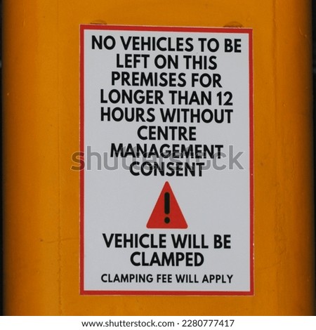 Vehicle will be clamped if left longer than 12 hours sign, on a yellow pole in a basement parking lot.