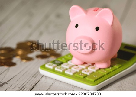 A piggy bank on a green calculator and coins on a wooden table. Close-up photo.
