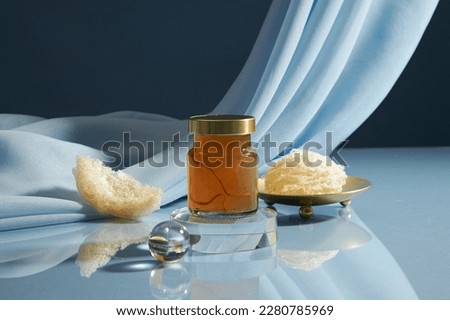 A glass bottle unlabeled containing bird’s nest water on transparent podium, some raw edible bird’ nest decorated on blue soft fabric background. healthcare food, front view, copy space Royalty-Free Stock Photo #2280785969