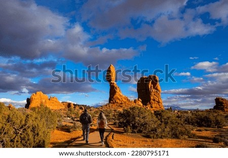 Couple hiking in red mountains. Friends walking on Balanced Rock trail.  Moab, Arches national Park, Utah, USA. Royalty-Free Stock Photo #2280795171