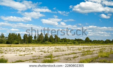 concrete runway of an abandoned airfield against a blue sky and clouds. Royalty-Free Stock Photo #2280802305