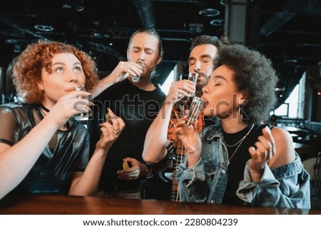 Multiethnic friends drinking tequila shots and holding fresh lime in bar Royalty-Free Stock Photo #2280804239