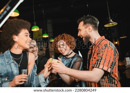 Cheerful friends holding lime and tequila near african american friend in bar Royalty-Free Stock Photo #2280804249
