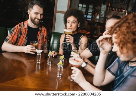 Multiethnic friends with cocktails and tequila shots spending time in bar at night