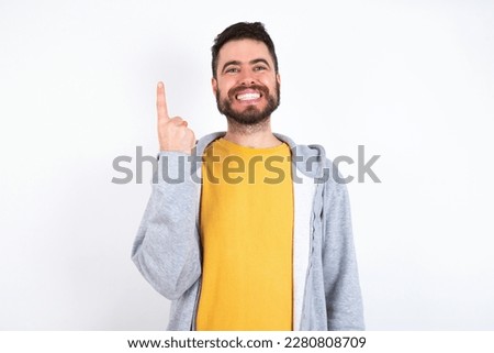 Young caucasian mán wearing trendy clothes over white background smiling and looking friendly, showing number one or first with hand forward, counting down