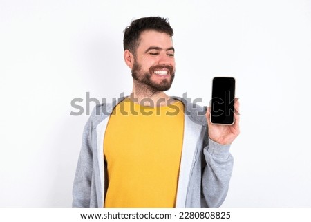 Photo of astonished crazy Young caucasian mán wearing trendy clothes over white background hold smartphone dislike feedback concept