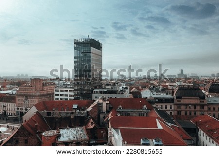 A modern glass building stands out amidst the red roofs of older buildings in this aerial view of Zagreb