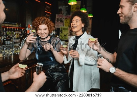 Cheerful multiethnic people having fun and holding tequila shots in bar Royalty-Free Stock Photo #2280816719
