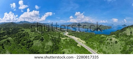 Aerial view of road in green meadows and hills. Top view from drone of rural road, mountains. Beautiful landscape with roadway, green grass, sky with clouds in Golo Mori - West Manggarai Regency Royalty-Free Stock Photo #2280817335
