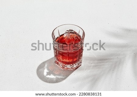 Classic cocktail negroni on white background with shadow, palm leaves and empty place. Negroni cocktail in glass in minimal style. Summer drink menu. Alcohol drink in tropical style in sunshine day. Royalty-Free Stock Photo #2280838131