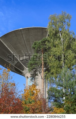 A water tower surrounded by trees with colourful leaves in Roihuvuori district in Helsinki, Finland. Interesting concrete architecture. Industrial fall landscape. Autumn urban picture.