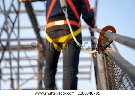 Working at height equipment. Fall arrestor device for worker with hooks for safety body harness on selective focus. Worker as a background. Royalty-Free Stock Photo #2280848785