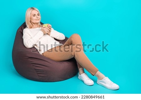 Full length photo of dreamy cute lady dressed white shirt sitting bean bag drinking tea empty space isolated teal color background