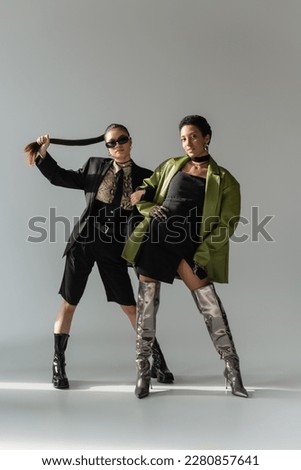 Fashionable interracial models in boots and spring clothes posing on grey background with sunlight