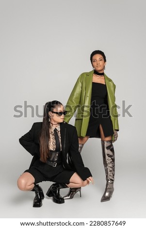 Trendy interracial girlfriends in spring clothes posing on grey background