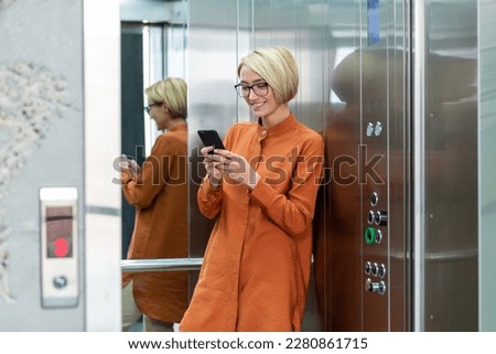Young beautiful woman inside office building at workplace working, businesswoman using phone standing in elevator, smiling and happy female worker starts new successful day. Royalty-Free Stock Photo #2280861715