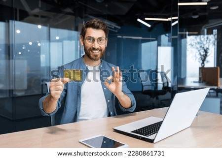 Successful businessman inside office building at workplace smiling and looking at camera, mature adult man holding and showing bank credit card, smiling contentedly. Royalty-Free Stock Photo #2280861731