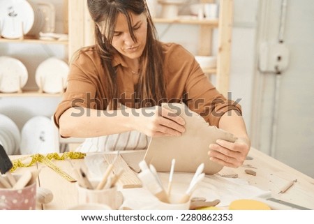 Woman painting and decorating a pottery in a ceramic workshop. Craft, art and hobbies concept.