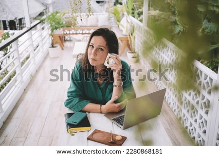 Portrait of skilled female IT professional with coffee cup looking at camera during time for remote job at balcone coworking, millennial woman with modern laptop computer for web networking posing