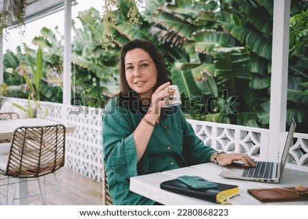 Portrait of skilled female IT professional with coffee cup looking at camera during time for remote job at balcone coworking, millennial woman with modern laptop computer for web networking posing