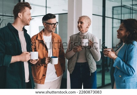Group of multiethnic colleagues standing with cups of coffee and looking at each other while taking coffee break and speaking about business strategy steps going forward in modern office Royalty-Free Stock Photo #2280873083