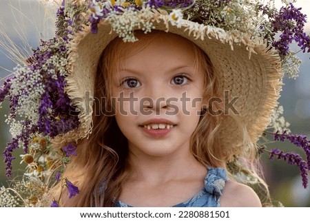Little girl wearing a hat decorated with wildflowers. Close-up.
