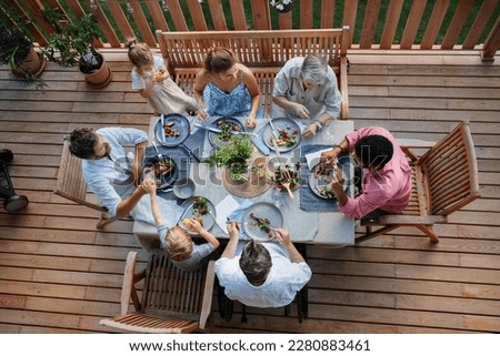 Top view of 3 generations family eating at barbecue party dinner on patio, people sitting at table on patio with grill. Royalty-Free Stock Photo #2280883461