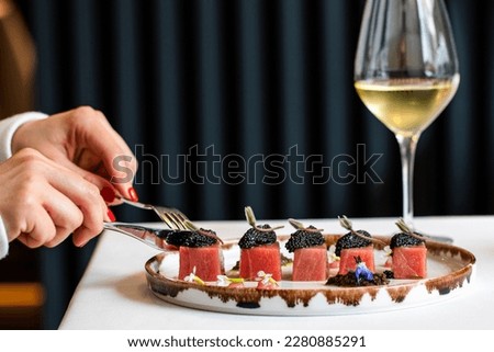Close up detail of female having dinner in top notch restaurant. Side view of female hands next to blue fin tuna dish with beluga caviar and a glass of white wine. Royalty-Free Stock Photo #2280885291