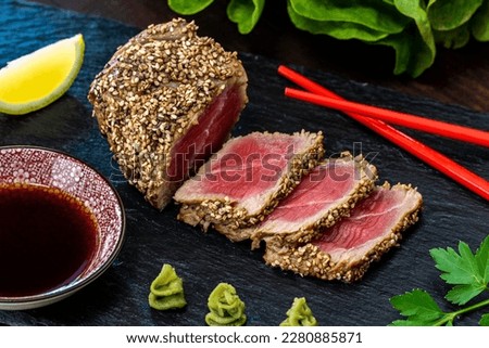 Close up of appetizing sesame crusted tuna steak. Medium rare Yellow fin tuna slices on black slate with wasabi, soy sauce and chopsticks. Royalty-Free Stock Photo #2280885871