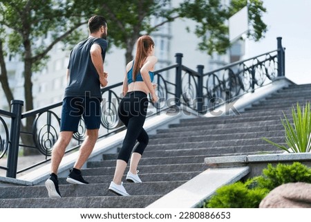 Image of happy smiling young couple, runners walking up or running on stone stairs, woman train with man, or bearded fit coach exercising, outdoors. Fitness, sport city, morning workout concept.