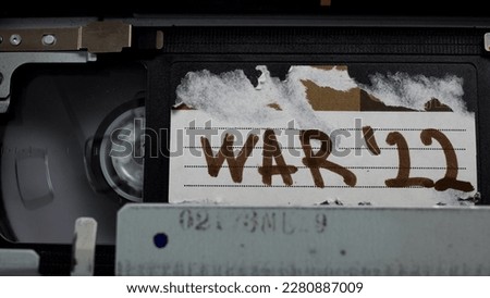 black cassette is inserted into old retro cassette player with inscription WAR 2022. VHS video cassette recorder put inside with old torn tag sign. Tape play documentary.