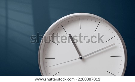 Nice metal hands of white clock go forward. wall clock shows time. Indistinguishable time, light from window on background.
