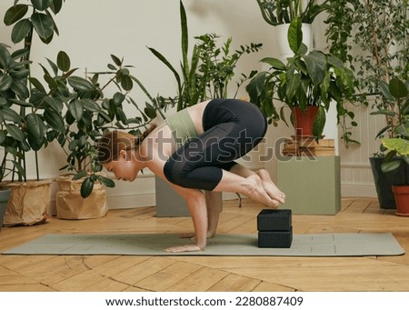 a woman does yoga at home performing an asana standing on her hands in a bright room full of plants