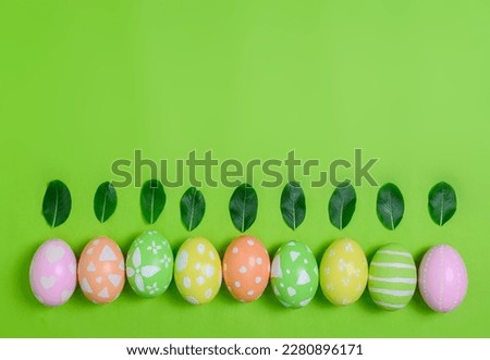 Happy Easter holiday greeting card concept. Colorful Easter Eggs and spring flowers on pastel green background. Top view, flat lay, copy space.