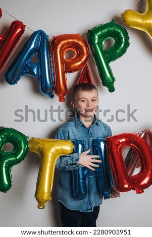 Children's birthday celebration. A joyful boy, a schoolboy, in a blue shirt against the background of colorful balloons. Front view
