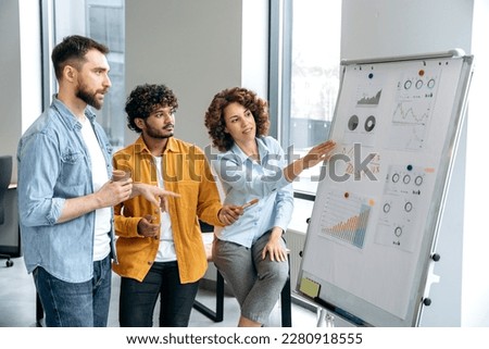Teamwork. Successful multiracial colleagues, stand in the office near a marker white board, analyze the results of work, financial statistic, predict financial risks and profitability in a boardroom Royalty-Free Stock Photo #2280918555