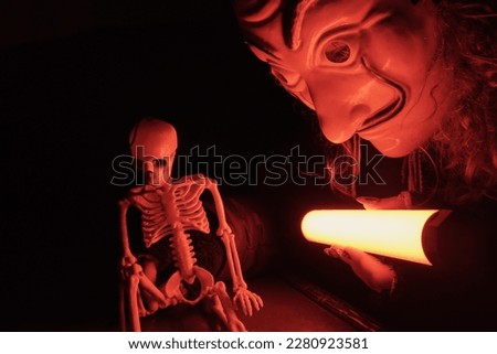 Photography of a skeleton in night. The man's improvised head bent over the table. A scientific experiment. A magic wand. Time travel. Dramatic red light. Close up photography
