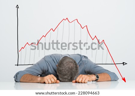 Depressed Businessman Leaning His Head Below a Bad Stock Market Chart Royalty-Free Stock Photo #228094663