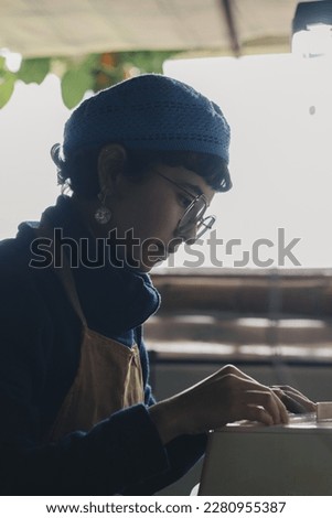 Detailed shot of a Craftsman girl working at her workshop. She wears glasses and a blue hat
