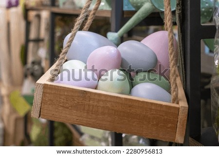 The beautiful large colorful Easter eggs in pastel colors in a wooden box with cotton ropes. Blurred shelf in the background.
