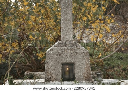 A nameless orthodox tombstone alone among the trees in autumn. An oil lamp is burning inside the tombstone