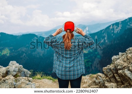 Woman in headphones listening music in nature and at the mountain, female tourist with long blond hair relax after walking enjoy journey trip, copy space