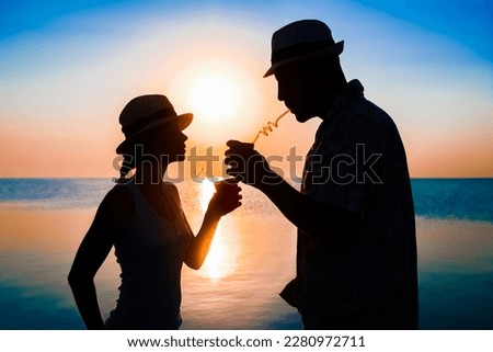 Happy couple drinking cocktail by the sea at sunset on travel silhouette in nature